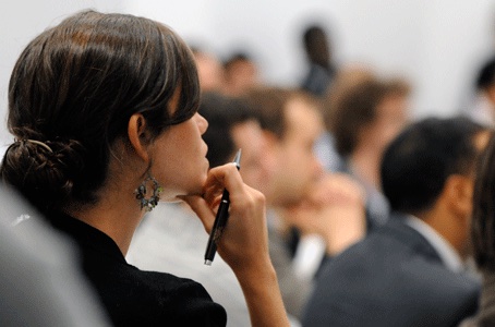 Person in classroom with chin resting on hand while holding a pen