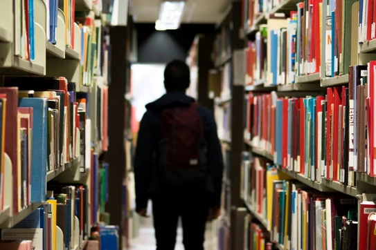 Student in a backpack walking between 2 shelves of library books