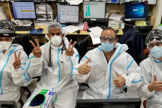 A group of healthcare workers wearing ppe throwing up peace signs and thumbs up.