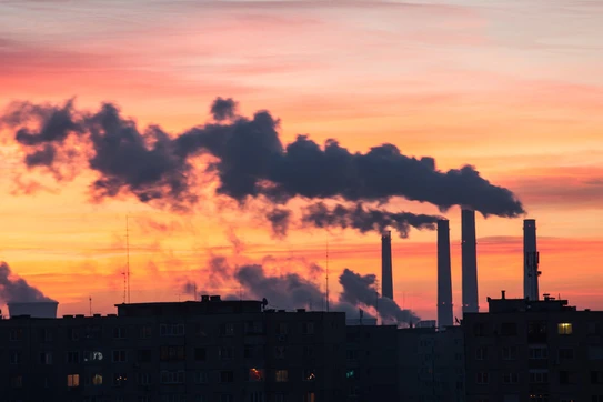 Smokestacks blowing smoke against a sunset 