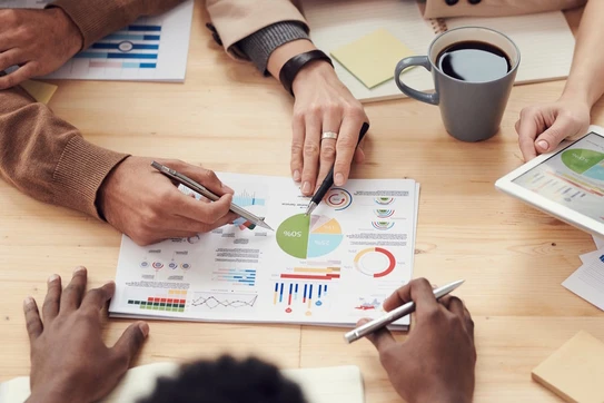 6 hands at a conference table, gesturing toward a pie chart