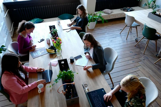 A group of women sitting around a wooden table photo. Photo by CoWomen on Unsplash.