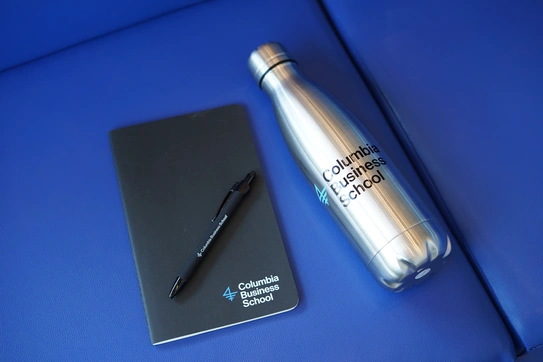 A CBS-branded notebook, pen, and water bottle rest on a bright blue couch cushion