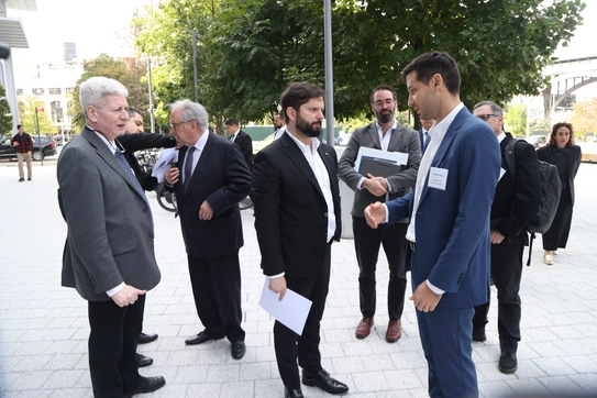 A cluster of men in suits gather outdoors, somewhere on the CBS campus