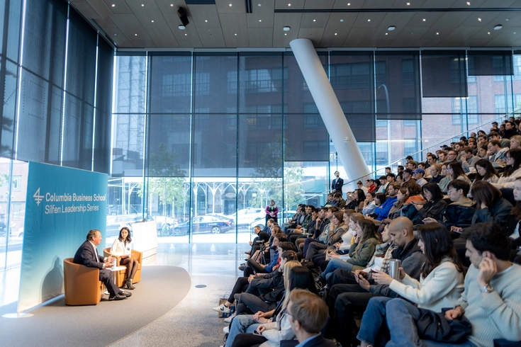Two people sit onstage in front of a full auditorium