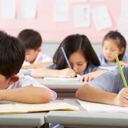 five school children writing at desks
