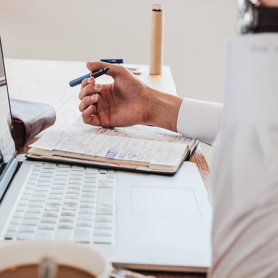 Person sitting at desk with their laptop, pen, and a notebook
