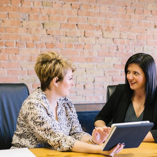 Image of two women sitting at a table speaking with a tablet
