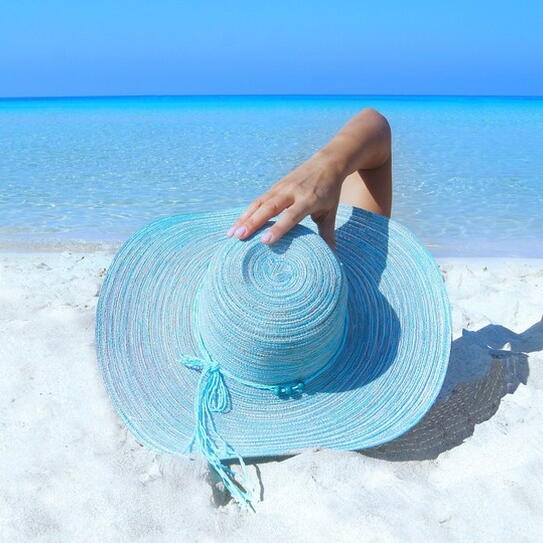 Woman laying on the sand at the beach wearing a blue wide brim hat